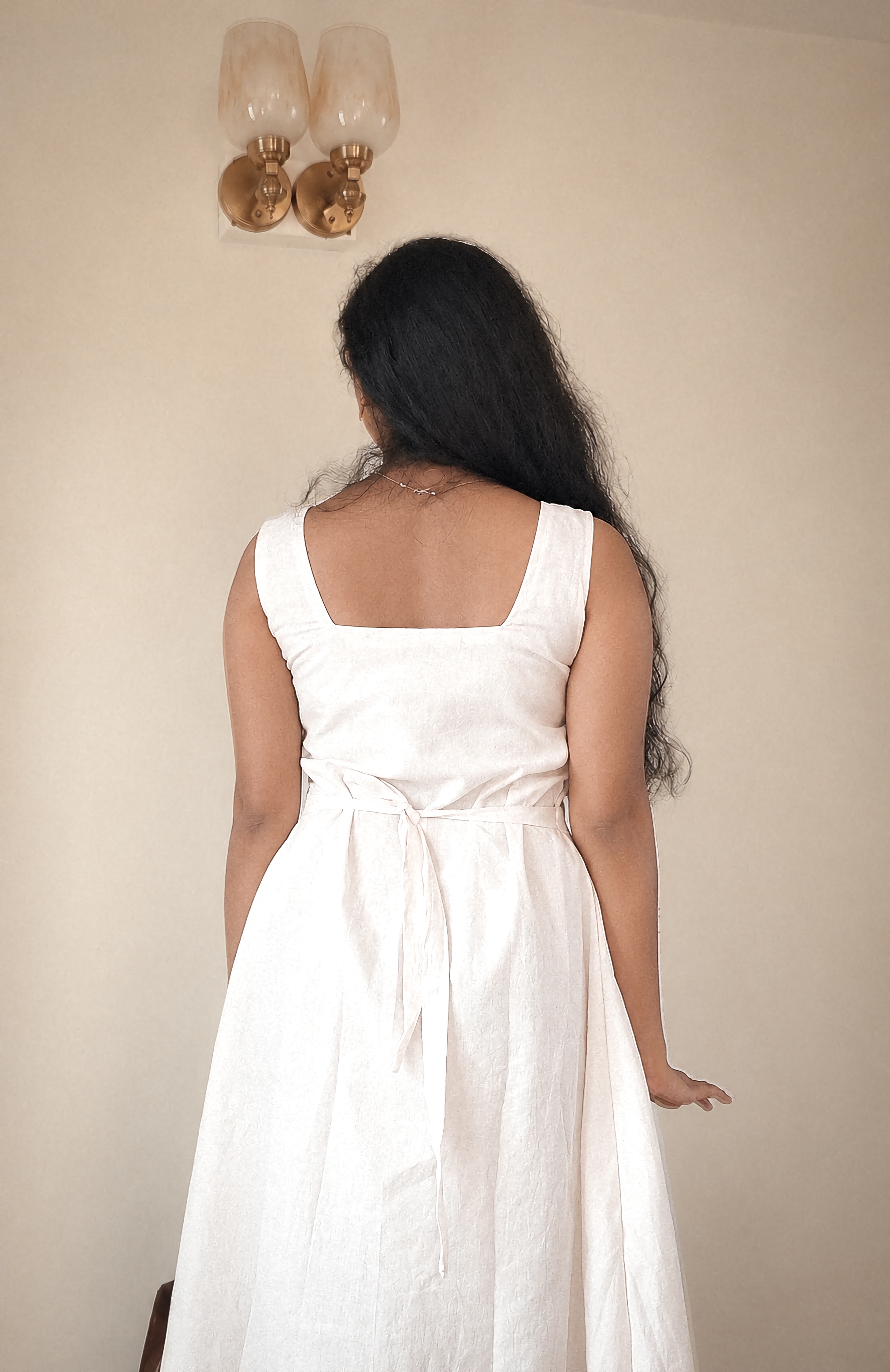 Back view of the Harshavi Chand ivory-white dress featuring a square back neckline, wide shoulder straps, an adjustable waist tie, and a flowing A-line skirt.