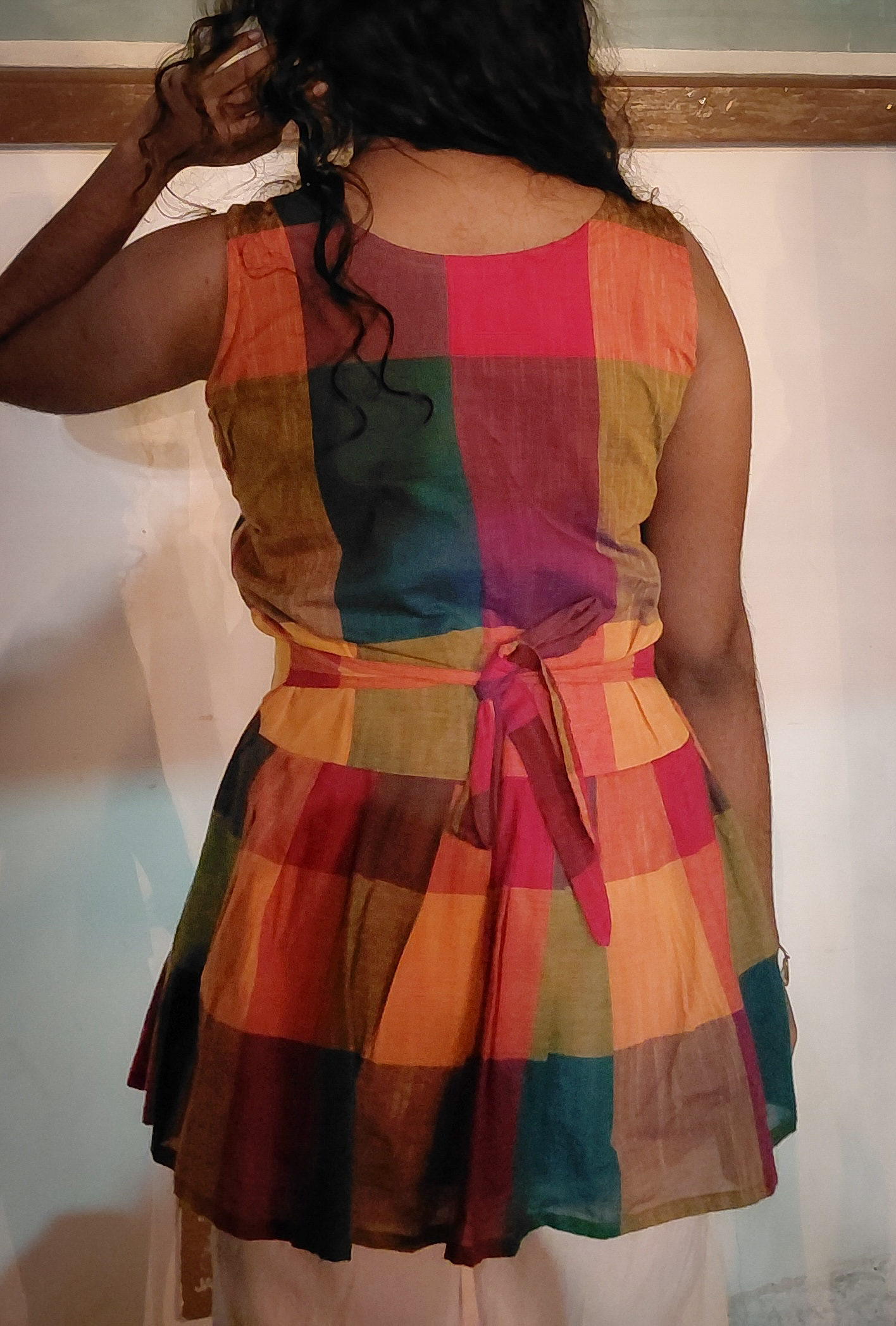 Back view of the Harshavi Madras Muse Dress featuring multicoloured Madras checks, a sleeveless design, a fitted waist with a tie-back detail, and a flared skirt.
